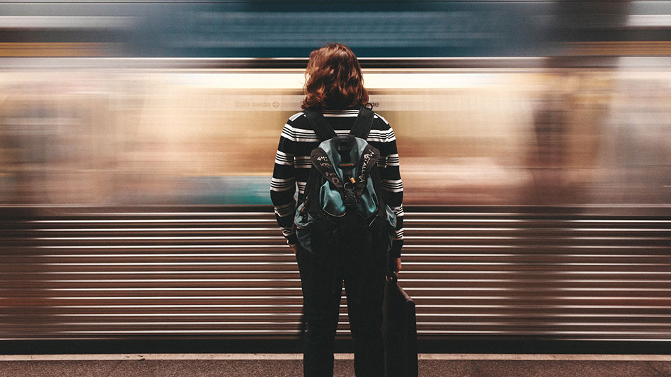 Person with long hair and backpack standing near a passing train